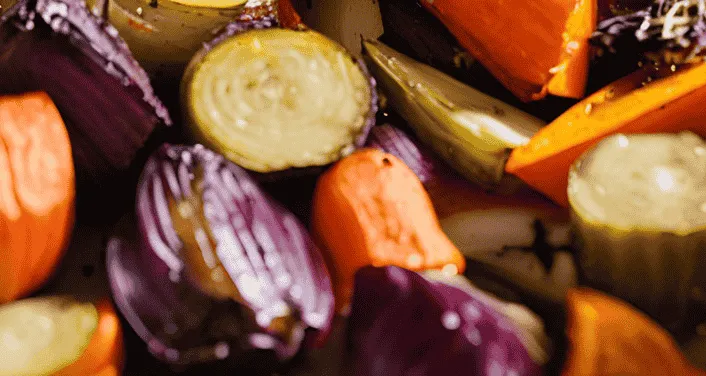 Close-up of colorful roasted vegetables, including carrots, zucchini, and red onions, with a golden sheen